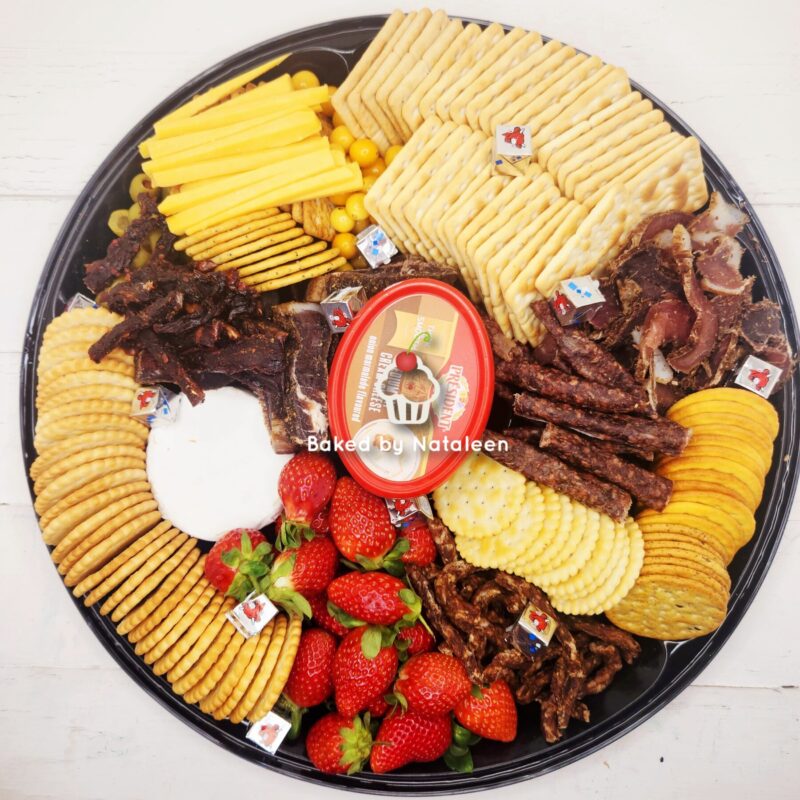 Large round platter piled with cheese slices, stacked crackers, beef jerky, round crackers, and fresh strawberries around a central red dip container.