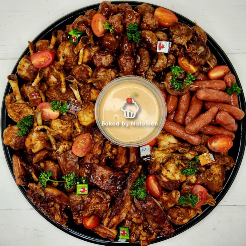 Round platter of mixed grilled meats (sausage, ribs, chicken bites) with tomatoes and parsley around a central creamy dipping sauce labeled 'Baked by Nataleen'.