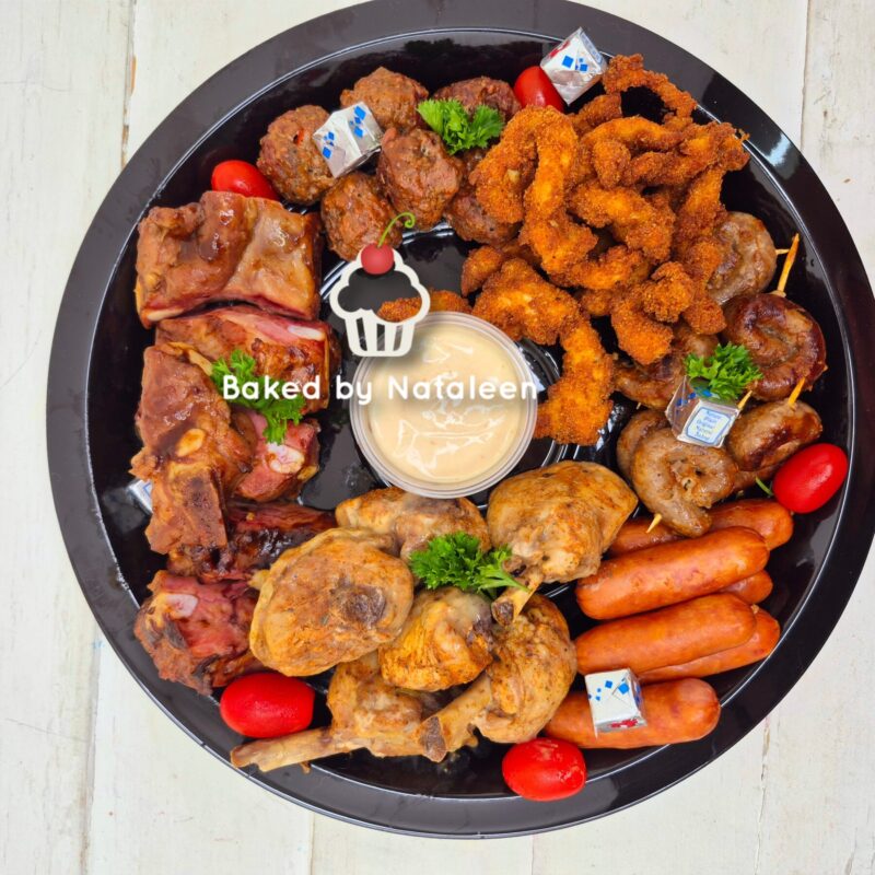 Round black platter with an assortment of fried and roasted bites: chicken wings, meatballs, onion rings, sausages, cherry tomatoes, and a central dipping sauce.