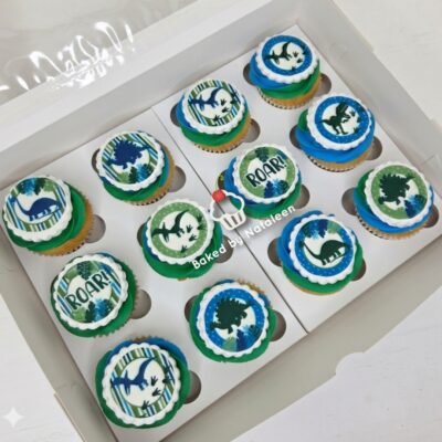 Box of dinosaur-themed cupcakes with blue and green frosting, edible toppers with dinos and ‘ROAR!’ messages in a white bakery box
