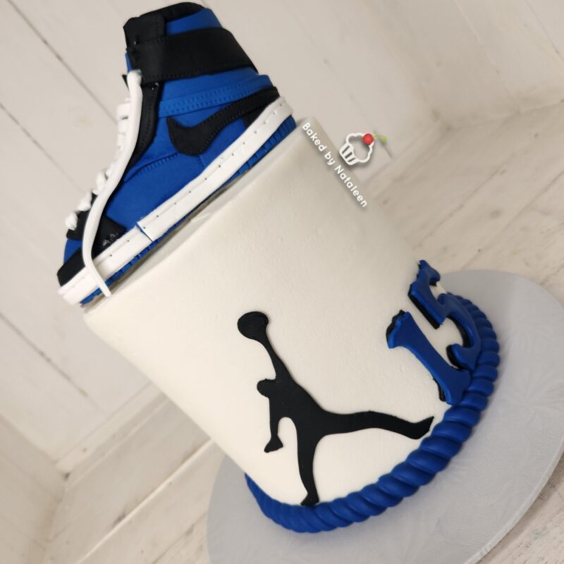White cake with a blue high-top sneaker topper and a black cat-like silhouette on the side in white fondant.