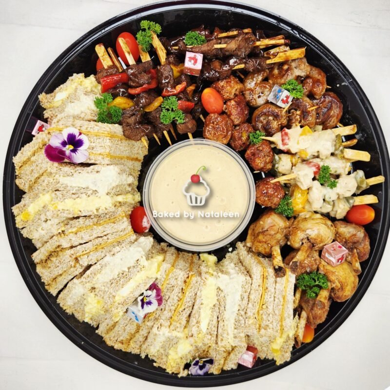 Large round platter with an assortment of skewered meats and vegetables, breaded cake slices, and a central dipping sauce labeled 'Baked by Nataleen'—garnished with parsley and edible flowers.