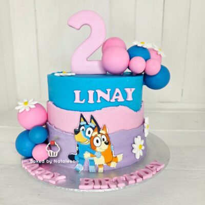 Two-tier pastel birthday cake with a large pink '2' topper, blue and pink layers, balloons, flowers, and cartoon characters on the side for a child’s celebration.