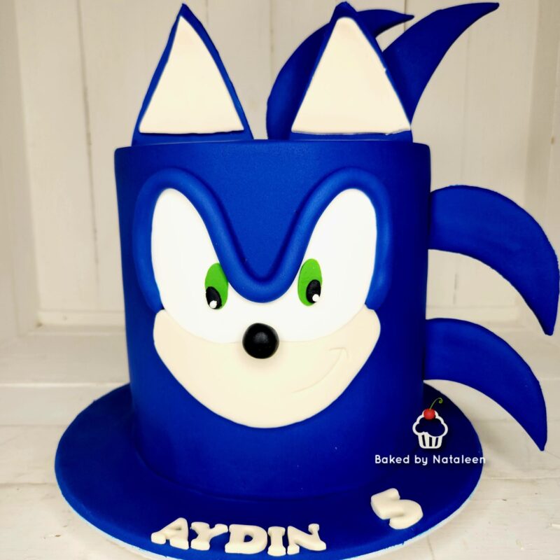 Bright blue Sonic the Hedgehog–inspired birthday cake with white eyes, green pupils, and a smiling muzzle on a round blue base.