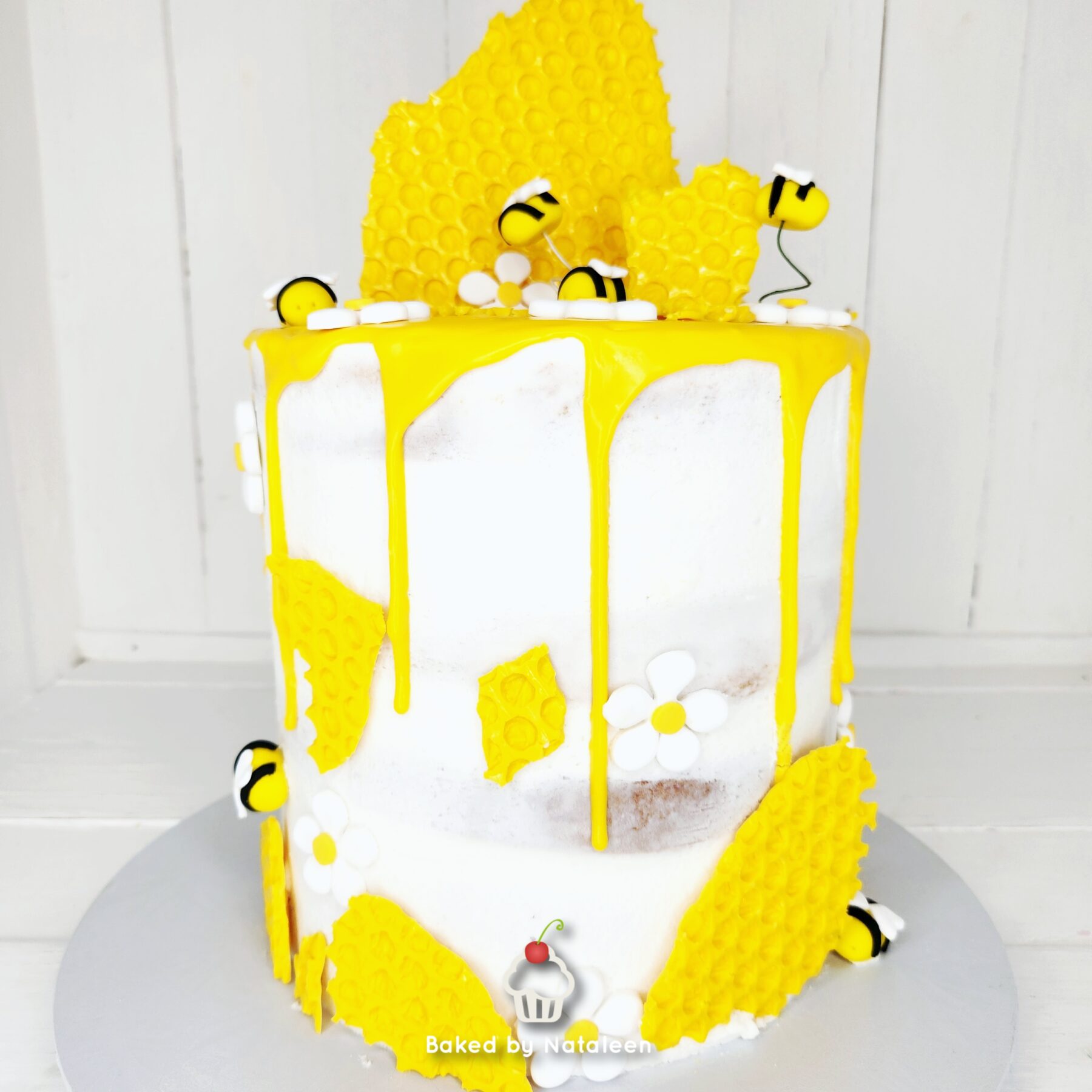 Tiered white cake with bright yellow drip icing and bee and daisy decorations.