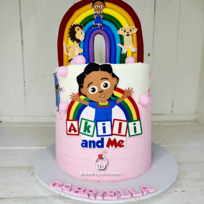 Two-tier birthday cake with a rainbow arch and Akili and Me characters, pink base, and 'Akili and Me' lettering on the front.