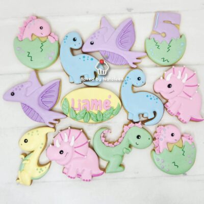 Assorted pastel dinosaur‑shaped cookies on a white wooden surface