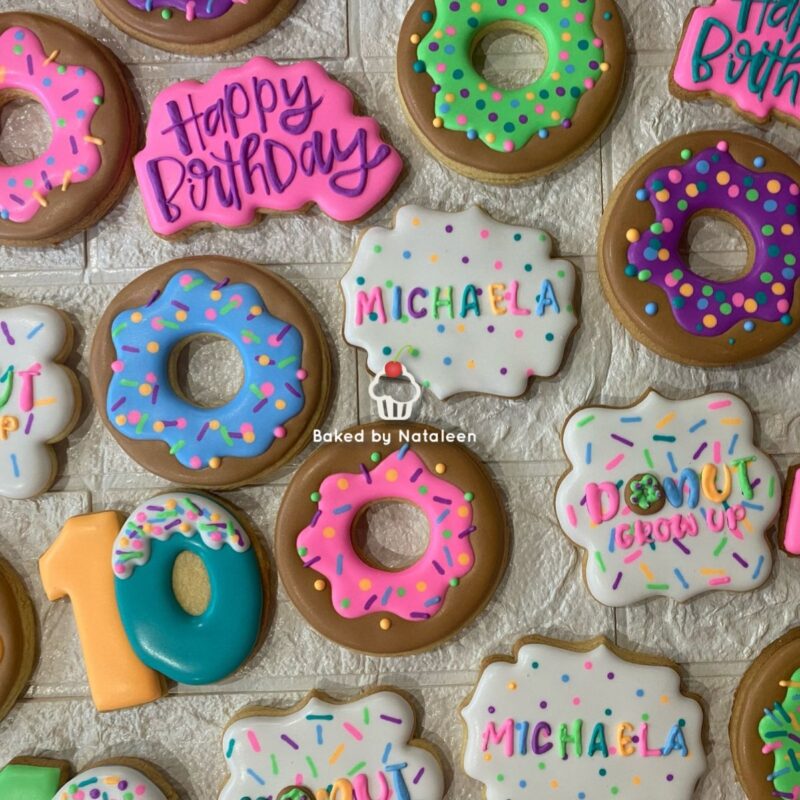 Colorful birthday cookies and donuts arranged on a white backdrop, with 'Happy Birthday' and the name Michaela written in icing.