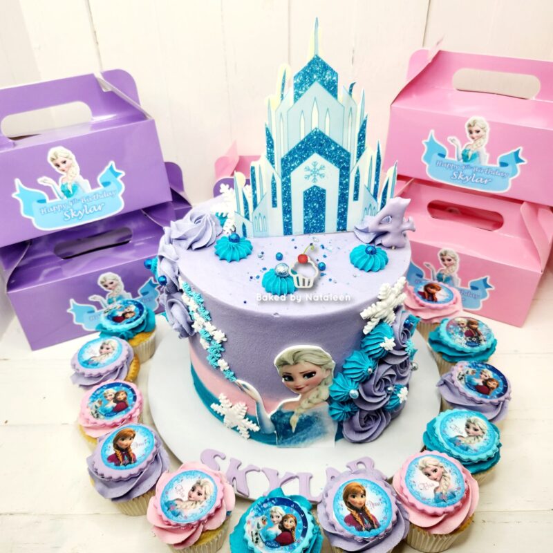 Frozen-themed birthday cake with a glittery ice castle topper, pastel purple and blue frosting, and matching cupcakes surrounding it.