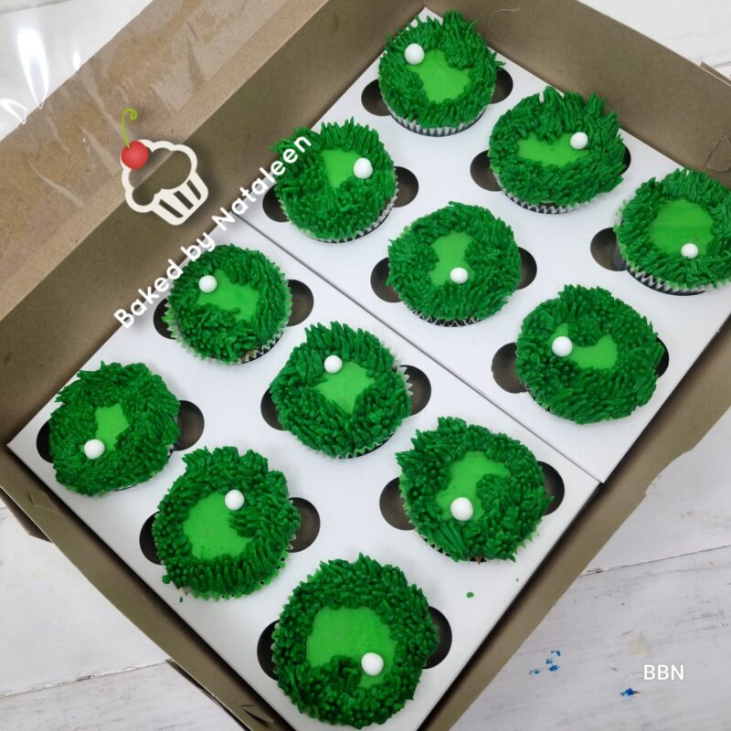 Green cupcakes with bright green frosting and a small white pearl, arranged in a white insert inside a cardboard bakery box.