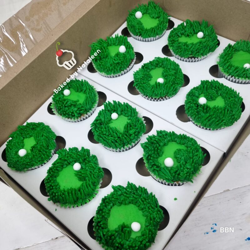Box of green grass‑frosted cupcakes with white sugar pearls, arranged in a white bakery box.