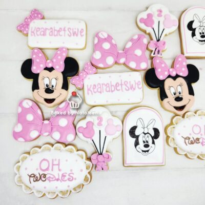 Assorted Minnie Mouse-themed cookies in pink and white with bows, balloons, and cupcakes for a celebration display