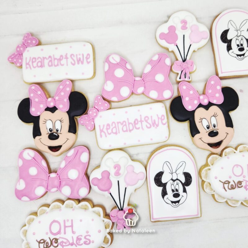 Assorted pink and white decorated cookies featuring Minnie Mouse faces, bows, balloons, and pastel speech bubbles.