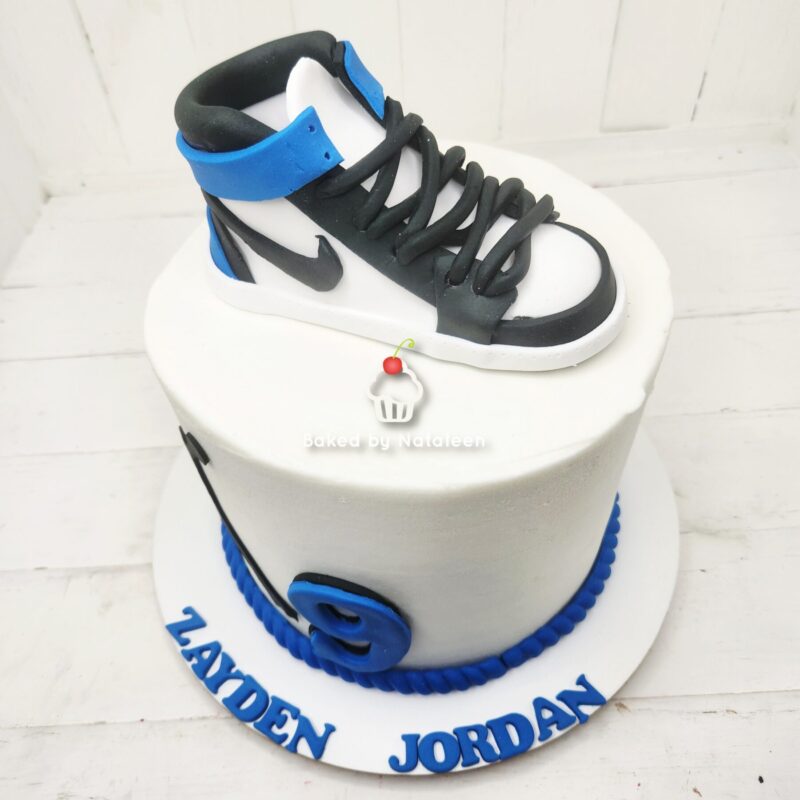White birthday cake topped with a black, white, and blue high-top sneaker fondant; blue "Zaiden Jordan" lettering on the base.