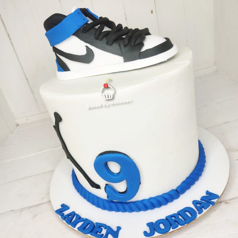 White birthday cake with a black-and-white Nike-style sneaker on top, a large blue number 9 on the side, and blue lettering spelling ZADEN JORDAN around the base.