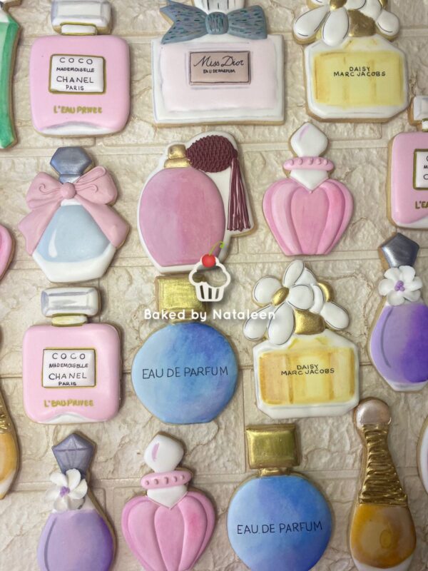 Assorted pastel perfume-bottle cookies with bows and flowers on a light brick backdrop, watermark 'Baked by Nataleen'