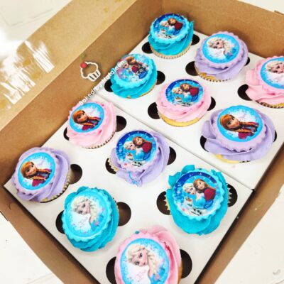 Box of Frozen-themed cupcakes with blue, pink, and purple swirled frosting and character toppers.