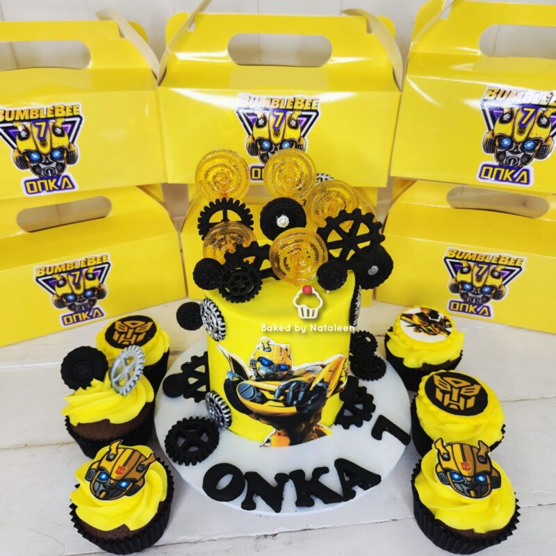 Yellow Bumblebee-themed cake with gears and cupcakes, surrounded by yellow Bumblebee Onka boxes for a party.
