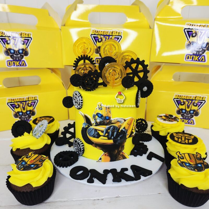 Yellow Bumblebee Transformers cake with gear decorations and matching cupcakes, boxes in background.