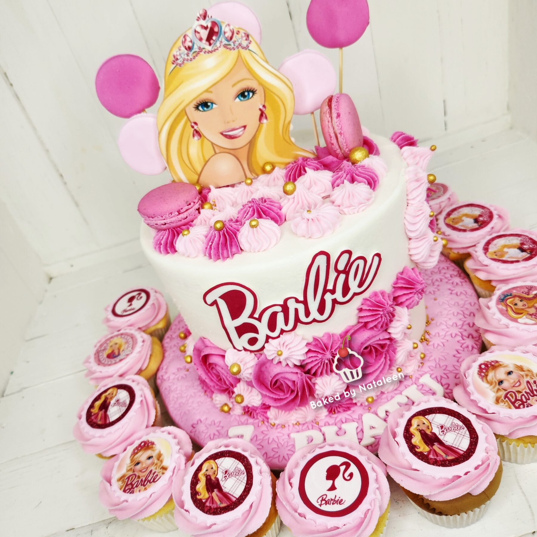Barbie-themed birthday cake with pink frosting swirls, a Barbie topper, macarons, and gold sugar beads.