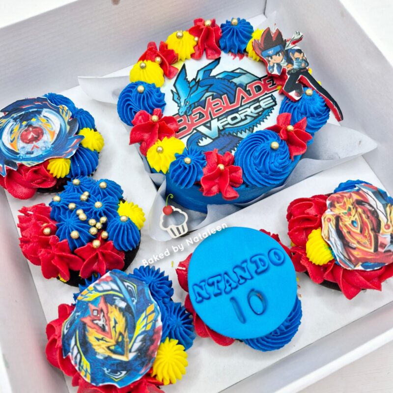 Assorted Beyblade-themed cupcakes in blue, red, and yellow with character toppers and a Beyblade Burst logo in a white box.