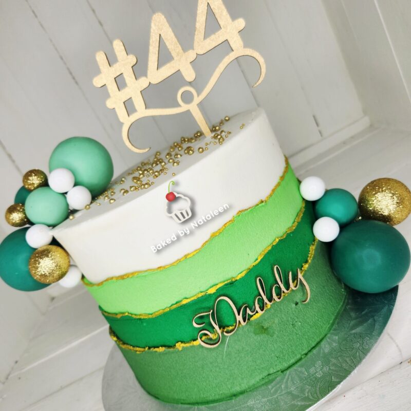 Three-tier cake with white, lime green, and dark green layers, gold trim, teal and gold decorative spheres, 'Daddy' on the front, and a gold '#44' topper.