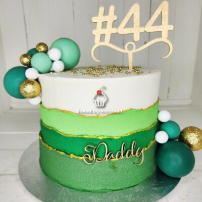 Two-tone green and white birthday cake with gold trim, a large '#44' topper, green/teal spheres, and 'Daddy' on the side.