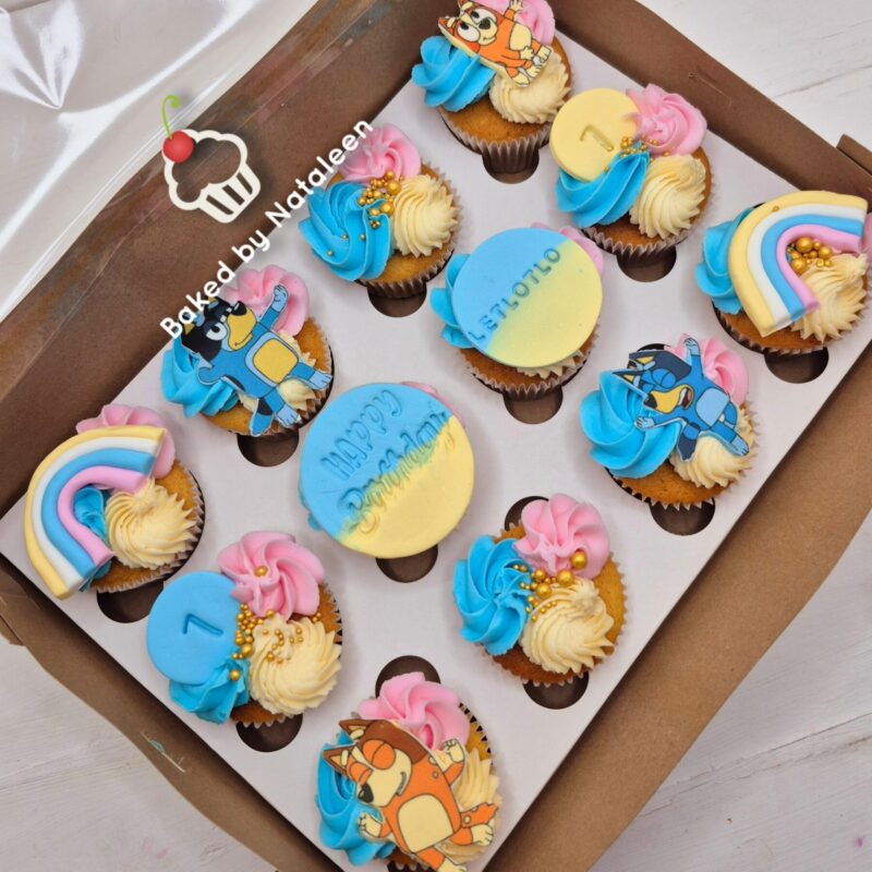 Box of colorful cupcakes with pastel frosting swirls and cute cartoon toppers in a white tray