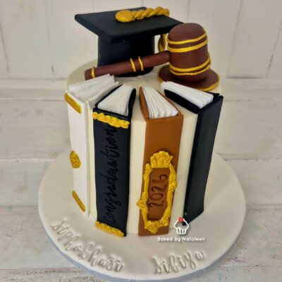 Cake decorated with edible book spines, graduation cap, and gavel on top; a diploma rolls by each book.