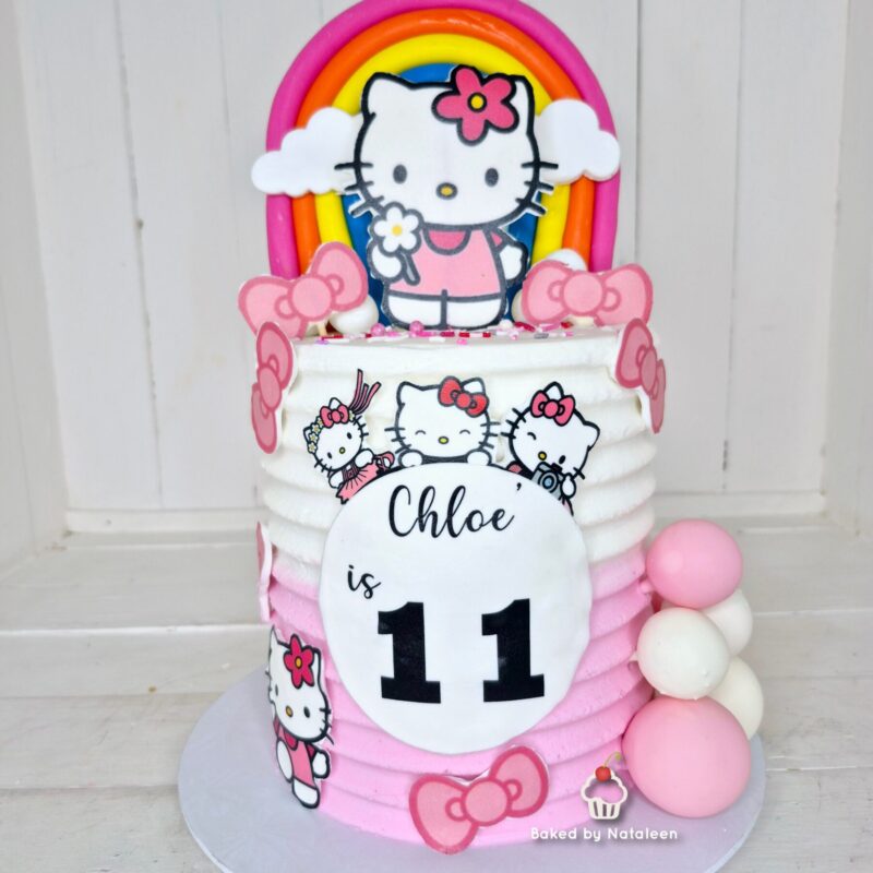 Hello Kitty birthday cake with pink and white frosting, a rainbow topper, and a large circular plaque that reads 'Chloe is 11'.