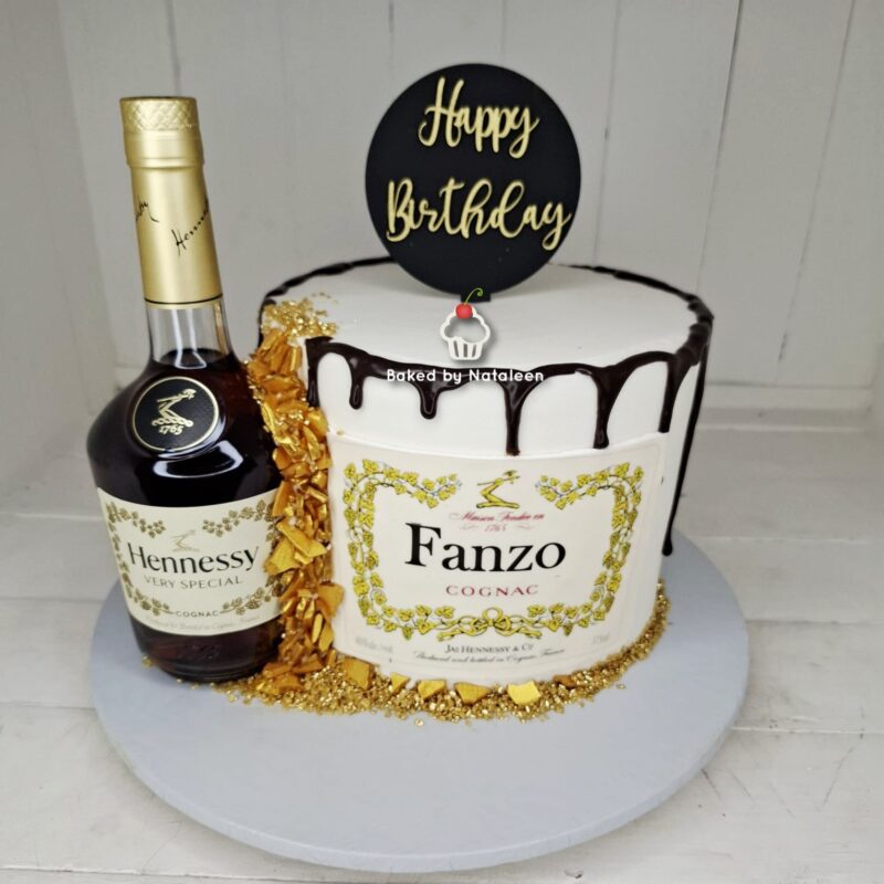 Birthday cake with white frosting and chocolate drip, gold accents, and a bottle of Hennessy beside it on the left.