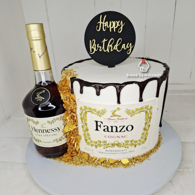 Birthday cake with chocolate drip, gold foil accents, and a round 'Happy Birthday' topper beside a bottle of Hennessy and a 'Baked by Nataleen' watermark.