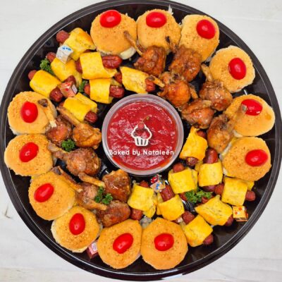 Round platter with bite-sized hors d'oeuvres around a central red dipping sauce; includes mini buns with cherry tomatoes, cheese cubes, and meat bites.