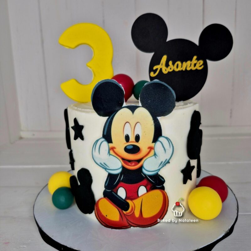 Birthday cake featuring Mickey Mouse decorations, a yellow '3' topper, and colorful candy balls around the base.