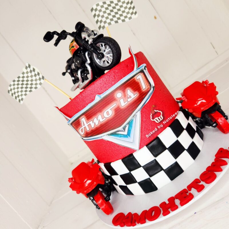 Racing-themed birthday cake with a motorcycle topper, black-and-white checkered flags, and bold red decorations