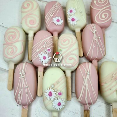 Assorted pastel pink and ivory cake pops on sticks, decorated with white drizzle and sugar daisies.
