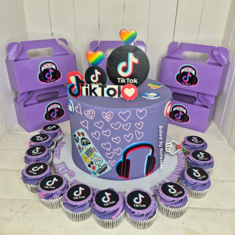 Purple TikTok-themed cake with heart decorations, headphones, and cupcakes arranged around it.