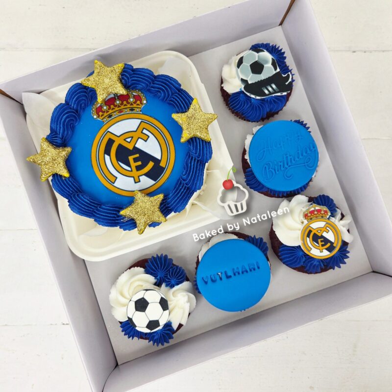 Blue birthday cake set featuring a Real Madrid crest cake with gold stars and six blue-frosted cupcakes with football toppers in a white box.