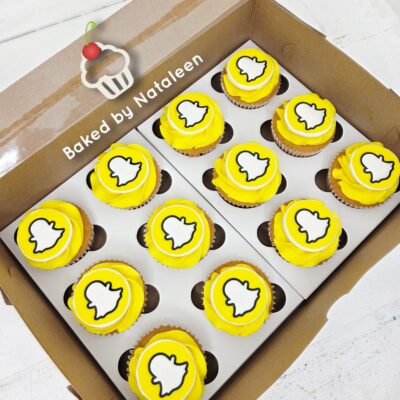 Box of yellow cupcakes with Snapchat ghost toppers, arranged in a bakery box labeled 'Baked by Nataleen'.