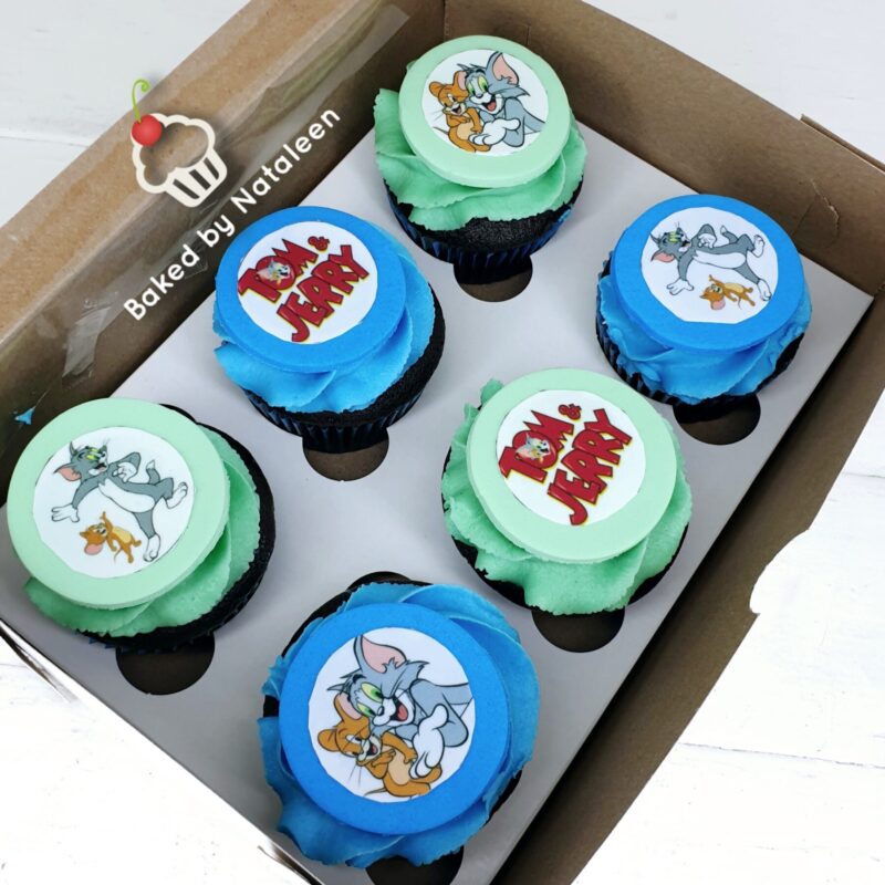 Six cupcakes in a brown box with blue and green frosting and circular toppers featuring Tom and Jerry characters and a 'Tom & Jerry' logo scene.