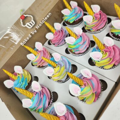 Box of rainbow cupcakes with golden unicorn horns and pink ears, in a bakery box labeled 'Baked by Nataleen' (informative)