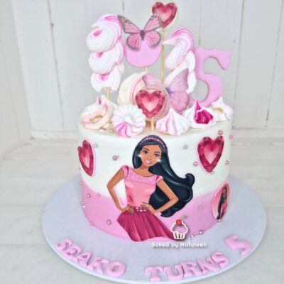 Pink-and-white birthday cake with heart gems and a Barbie illustration on the side, pink number 5 topper on top.