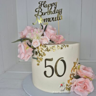 White fondant cake with pink roses and gold leaf accents, displaying a large '50' and a gold 'Happy Birthday' topper.