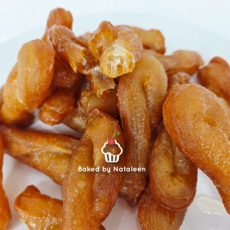 Pile of golden-brown fried dough twists on a white plate, close-up view, with a small amount of cream on the side.