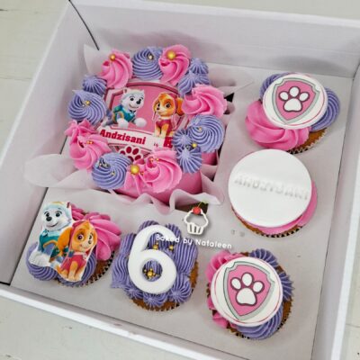 Paw Patrol themed birthday cake and cupcakes with pink and purple frosting, and a '6' cake topper in a white box box.