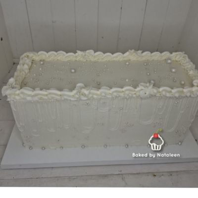Rectangular white cake with pearl decorations and a ruffled icing border; watermark says 'Baked by Nataleen' with a cupcake icon.
