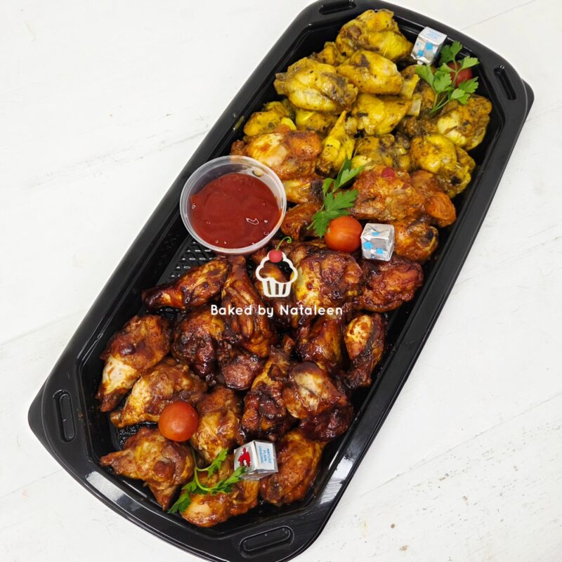 Assorted roasted chicken pieces in a black serving tray with a cup of red dipping sauce, cherries tomatoes, and parsley garnish. Watermark reads 'Baked by Nataleen'.