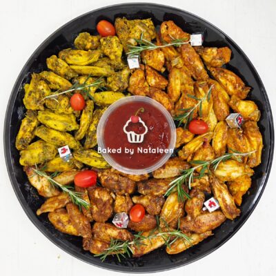 Round platter of assorted roasted wings and potatoes with cherry tomatoes and rosemary, centered around a red dipping sauce labeled 'Baked by Nataleen'.
