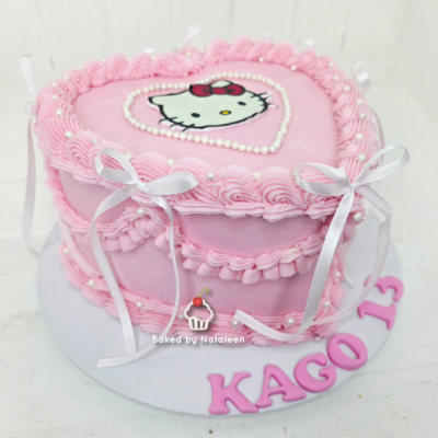 Pink heart-shaped birthday cake with Hello Kitty topper, white pearl border, and white fondant ribbons surrounding the sides.