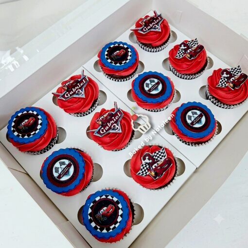 Box of twelve red-frosted cupcakes with blue accents and racing-themed toppers inside a white display box.